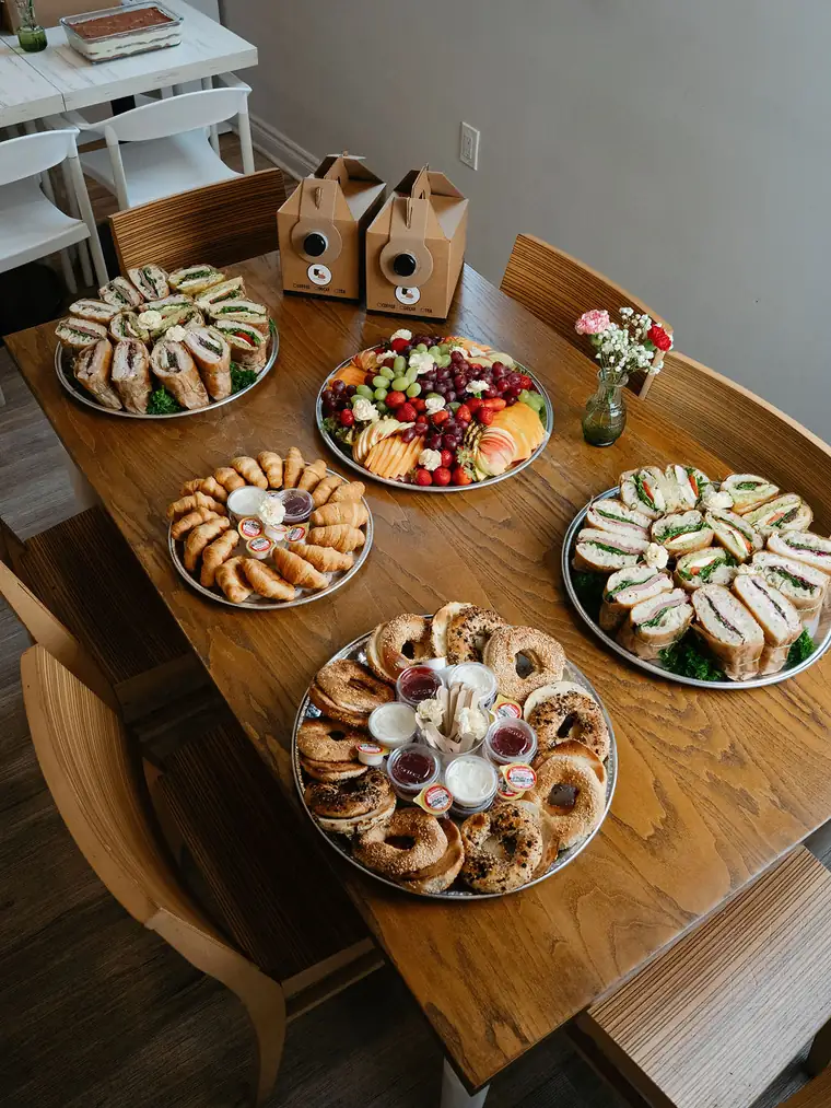Catering table set with sandwich trays, a fruit platter, croissants, bagels and two boxes of coffee