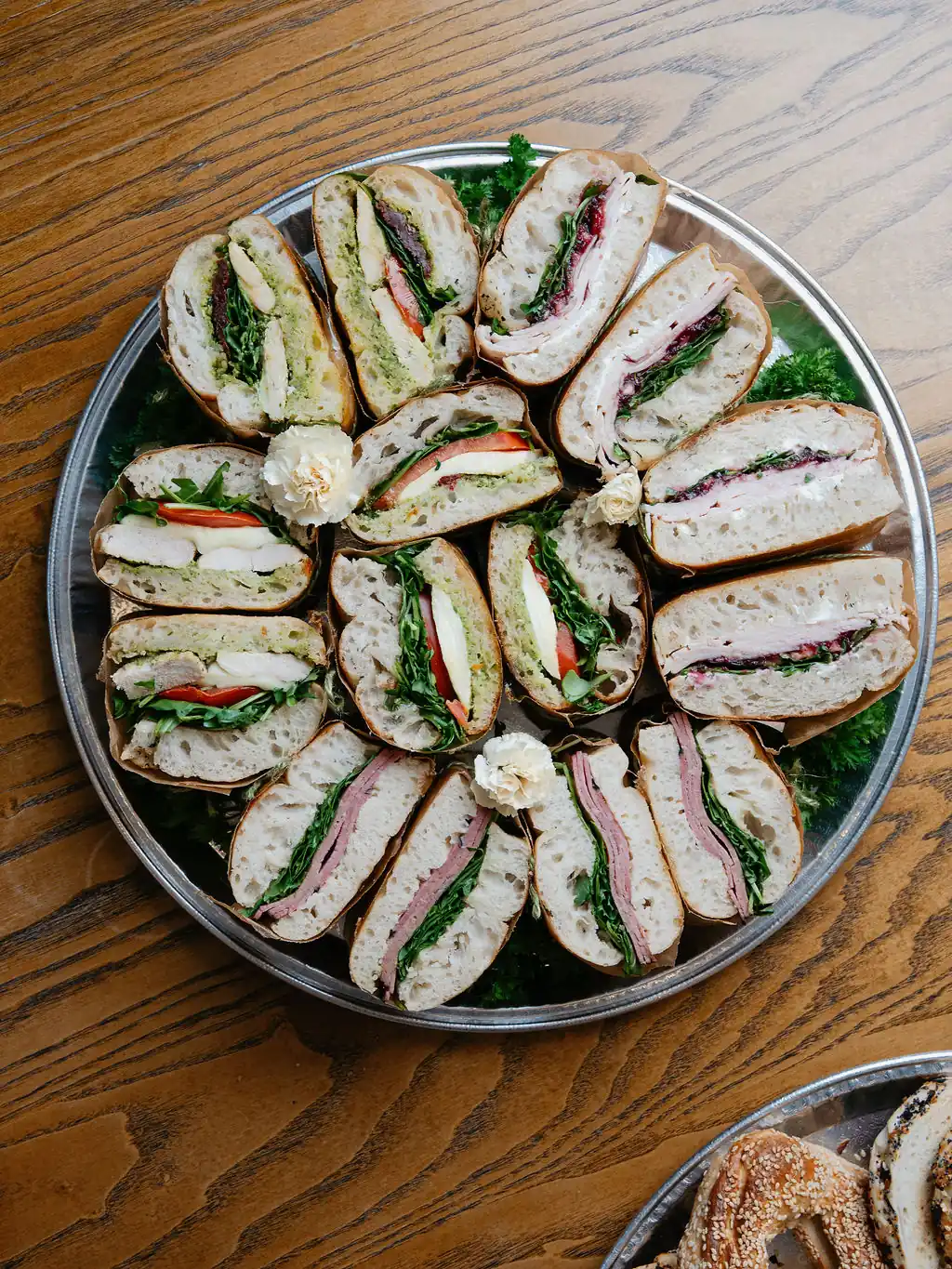 Round catering tray of sandwich halves on fresh ciabatta with greens, tomato and mozzarella